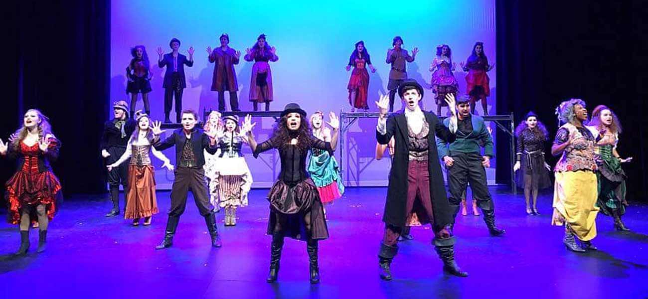 Large cast performing a theatrical production in elaborate costumes on stage